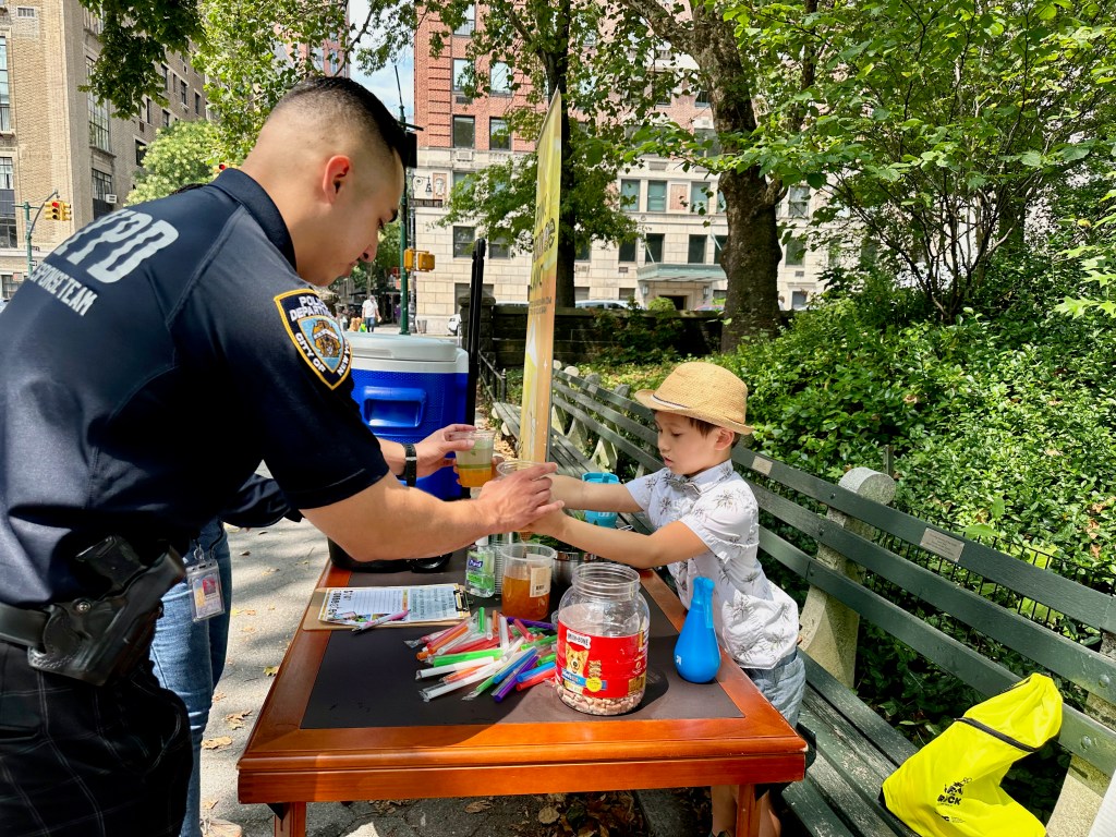 Julian Lin selling a cup of lemonade to a police officer at one of his lemonade stands on the Upper West Side