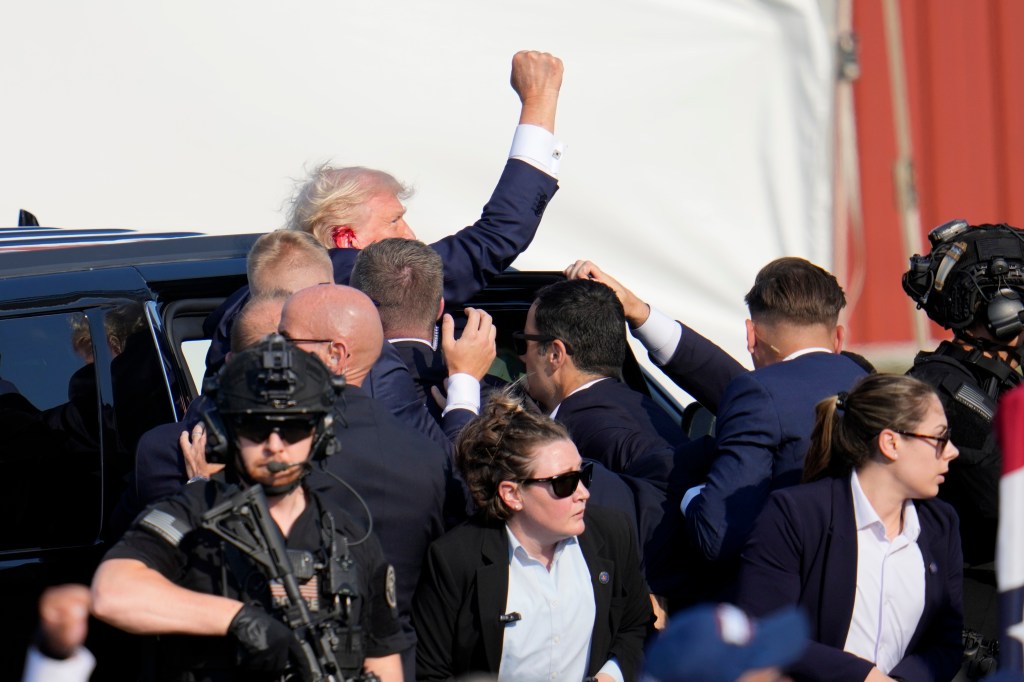 Donald Trump, injured, being escorted into a vehicle.
