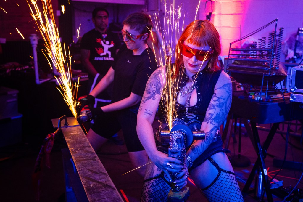 Two women using angle grinders during a performance, sparks flying.