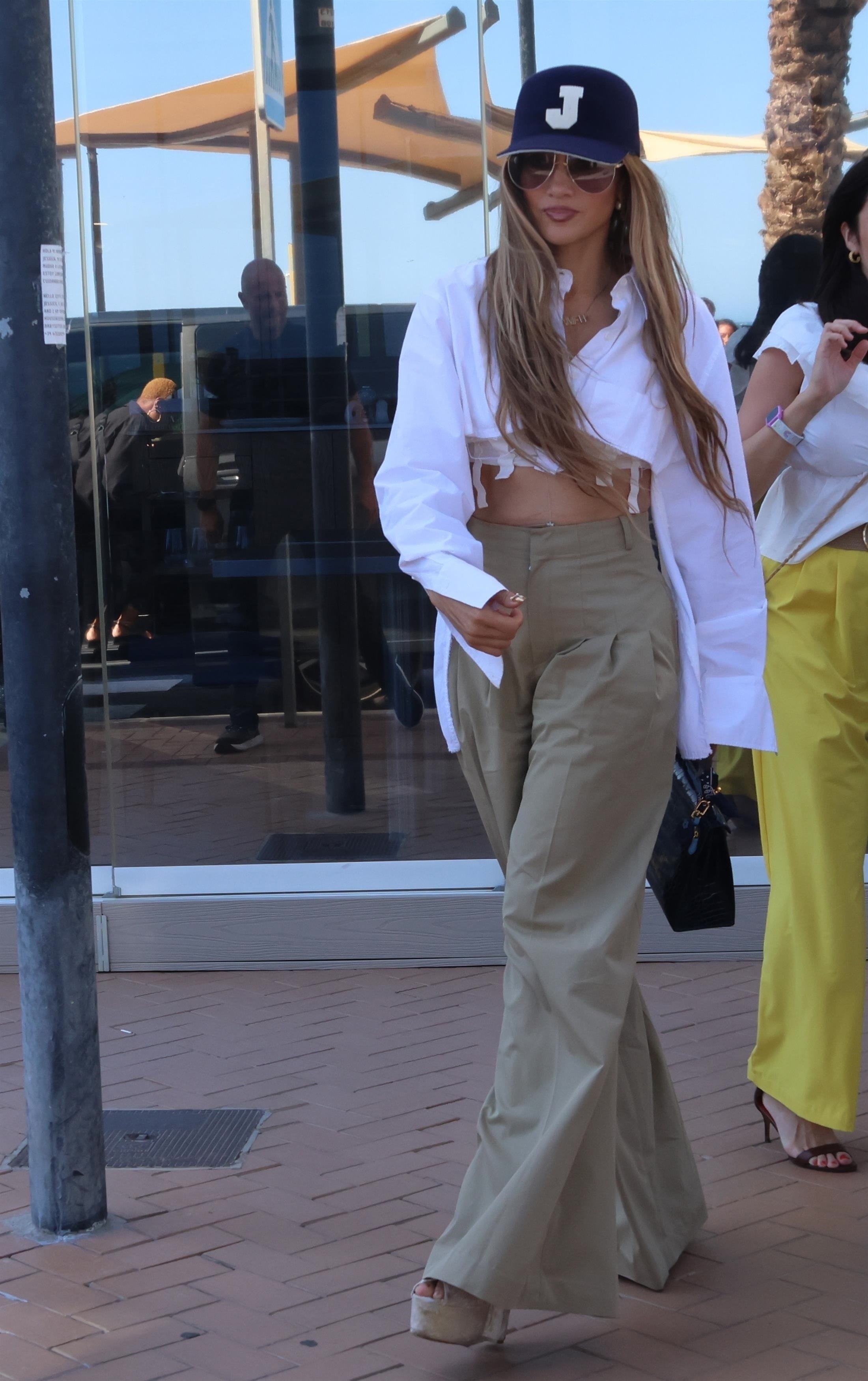 Jennifer Lopez in a white crop top and blue hat. 