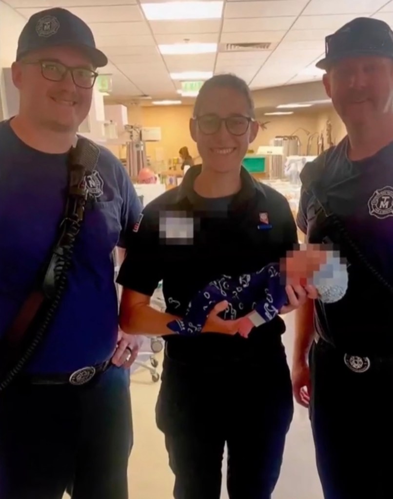 A firefighter holding a baby.  Two other firefighters stand on either side.