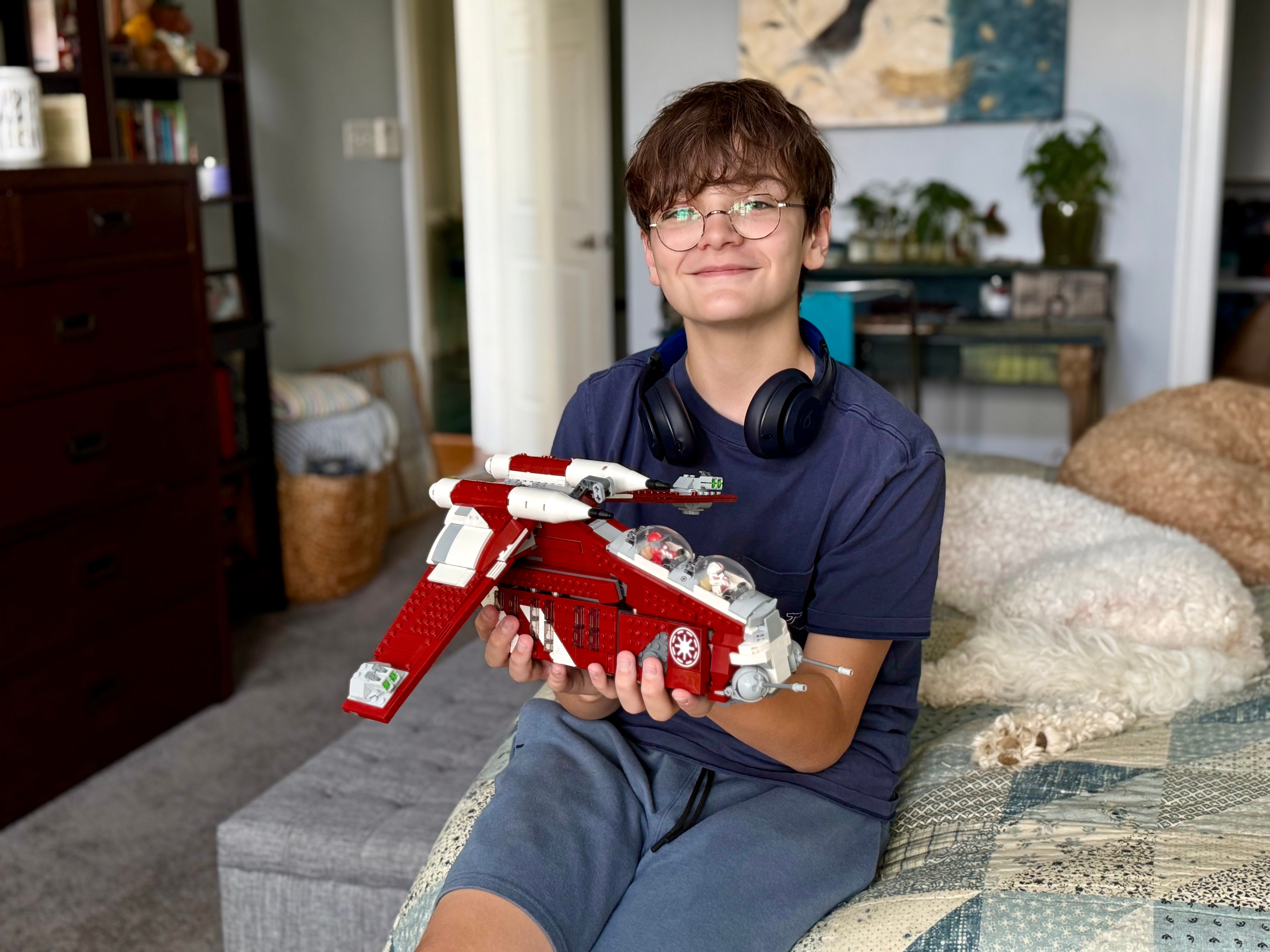 One of the author's kids holding a toy for the camera with headphones around their neck.