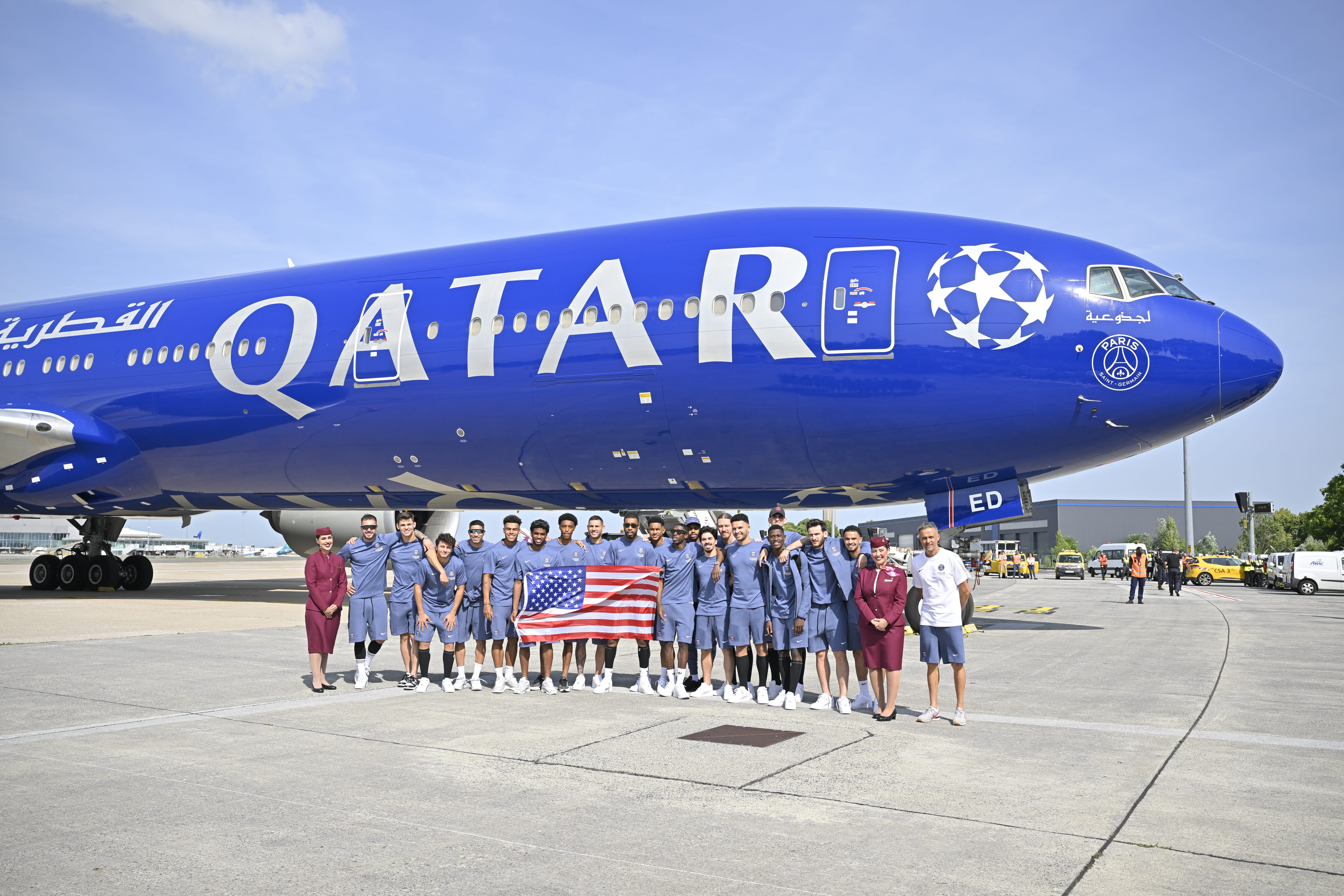 Paris Saint-Germain team members hold a USA flag in front of a Qatar Airways Boeing 777