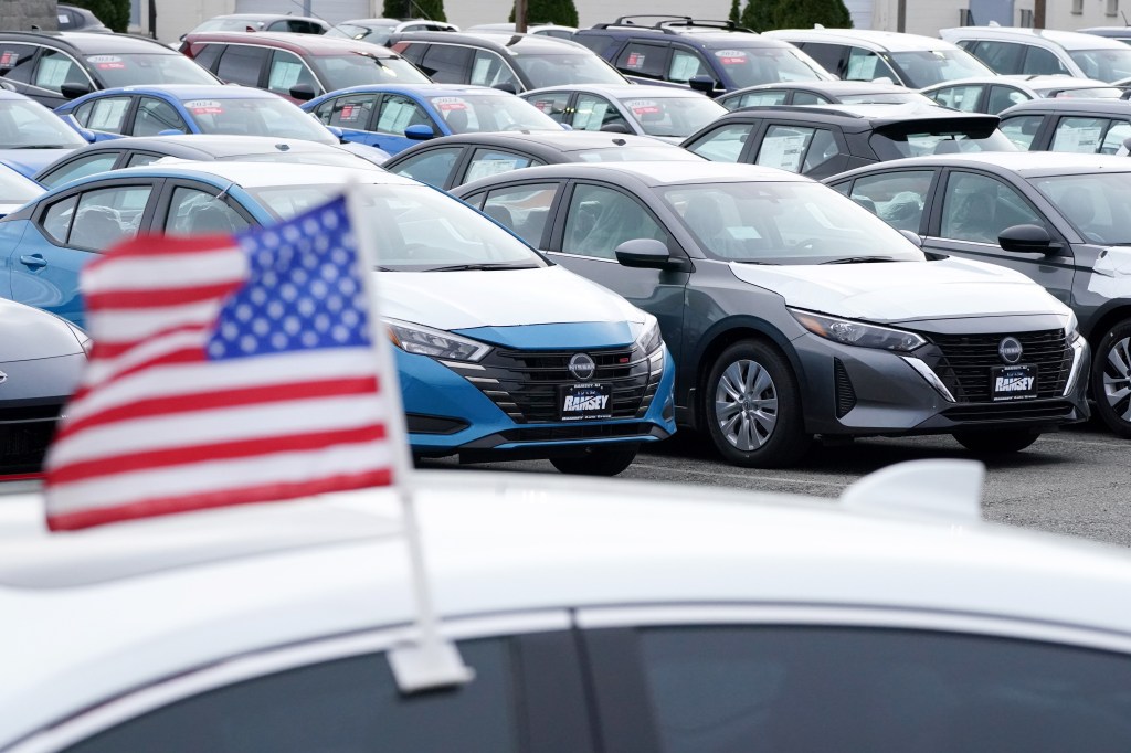 New Nissan cars at a dealership with an American flag in the foreground.