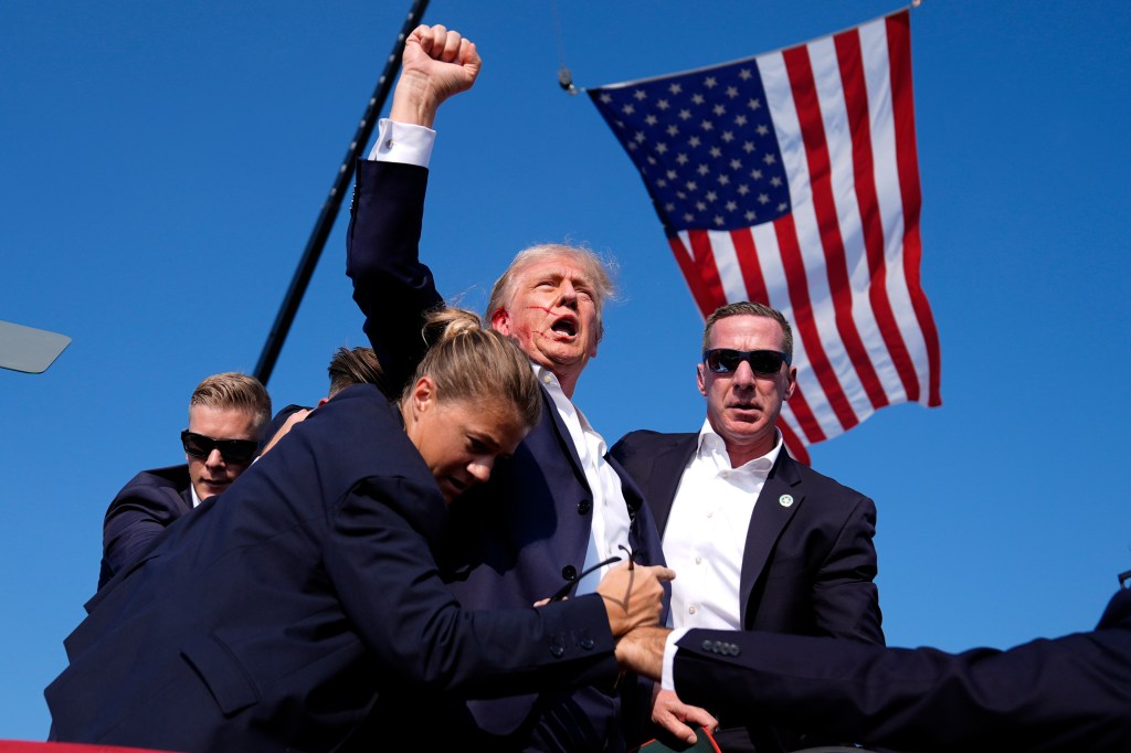 Donald Trump at a campaign rally, with Secret Service agents surrounding him.