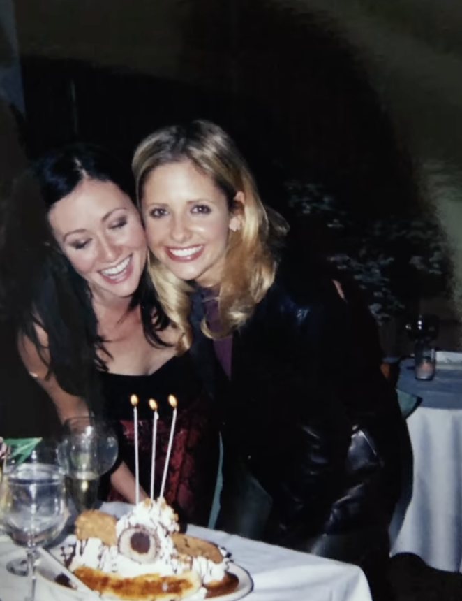 Shannen Doherty and Sarah Michelle Gellar getting ready to blow out candles on a dessert.