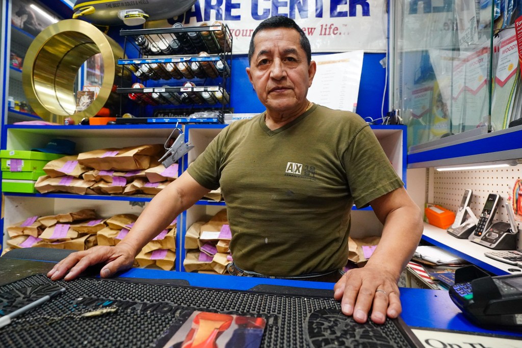 Man standing behind a shoe repair shop counter.