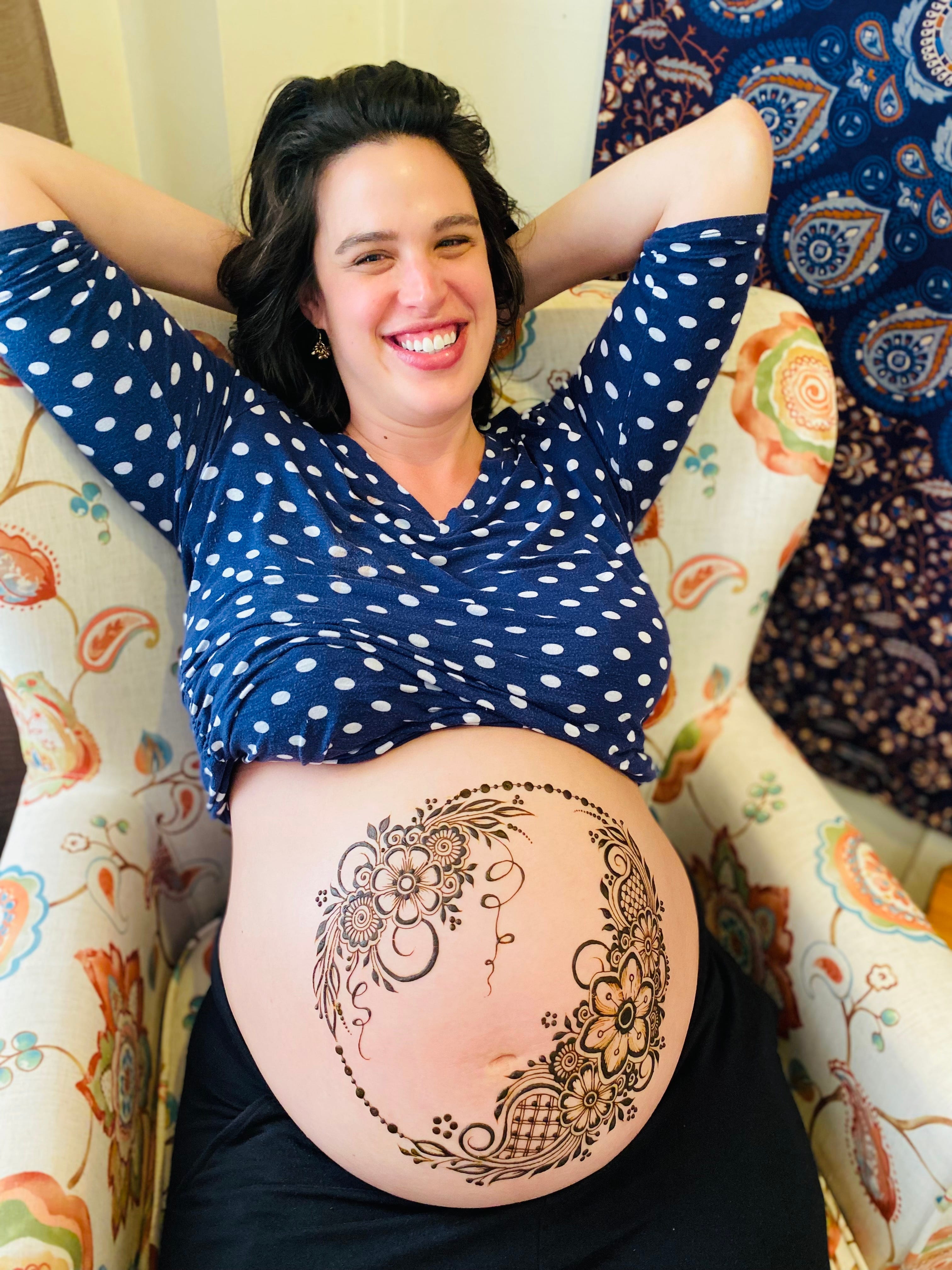 The author sitting back in a chair with a henna design on her pregnant belly.