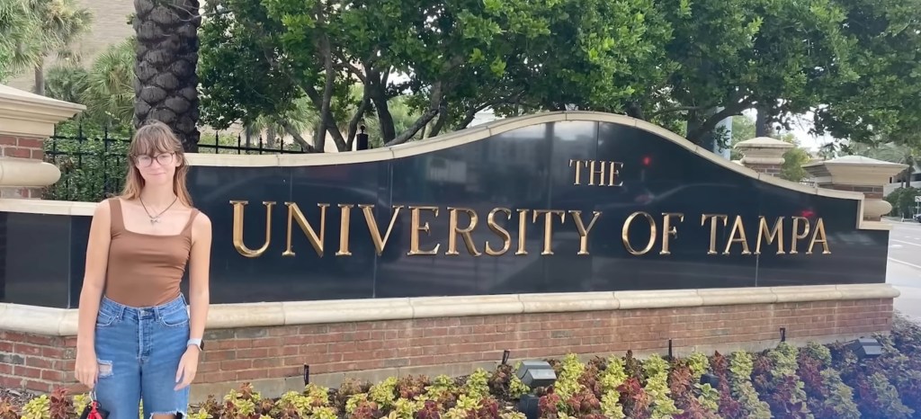 A woman standing in front of the University of Tampa sign.