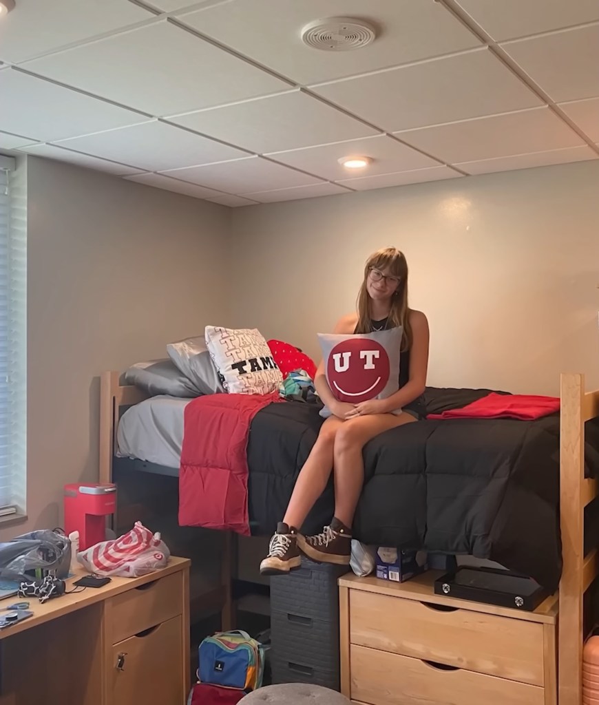 College student sitting on her bed in a dorm room.