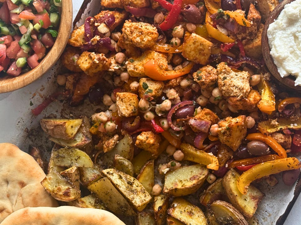 Roasted tofu and veggies on a sheet pan, served with a bowl of tomatoes and cucumbers, plus pita on the side.
