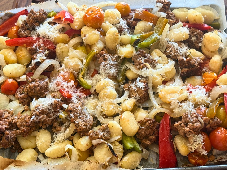 Gnocchi, sausage, peppers, and onions roasted on a sheet pan and sprinkled with Parmesan cheese.