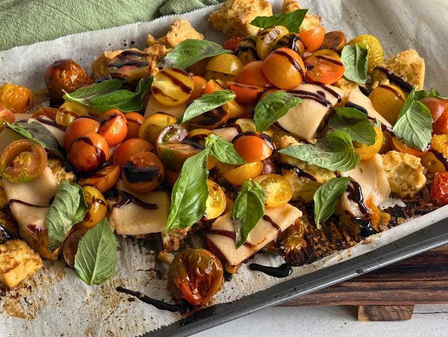 Tofu and tomatoes roasted on a sheet pan drizzled with balsamic glaze and garnished with basil leaves.