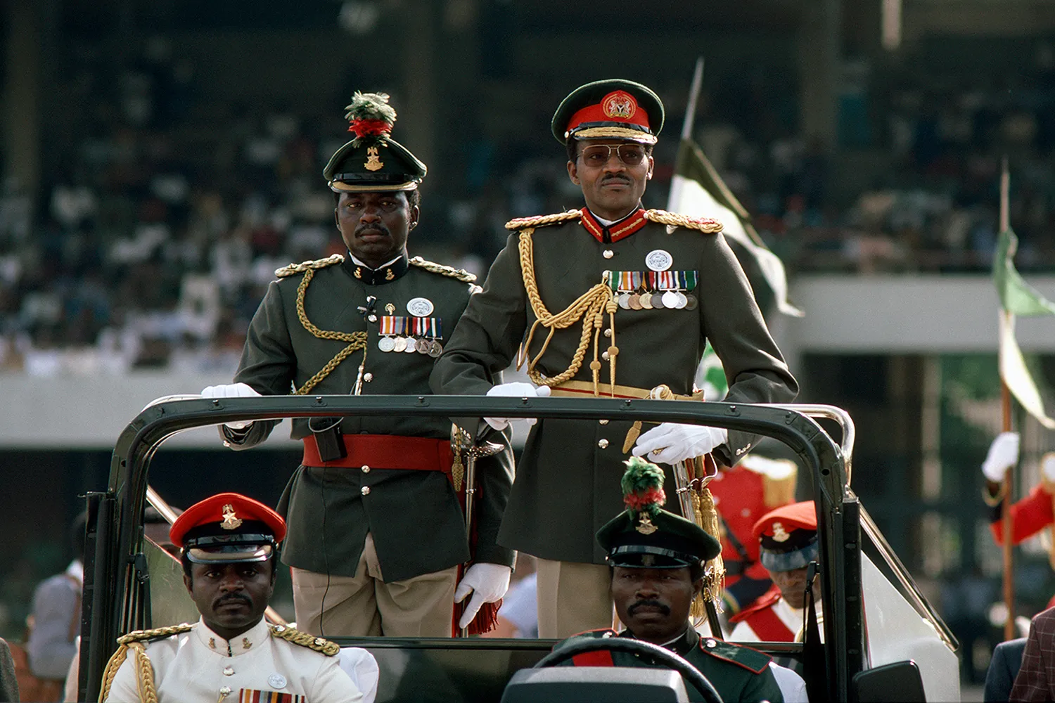 Muhammadu Buhari, dressed in uniform, rides in a military vehicle with others in uniform.