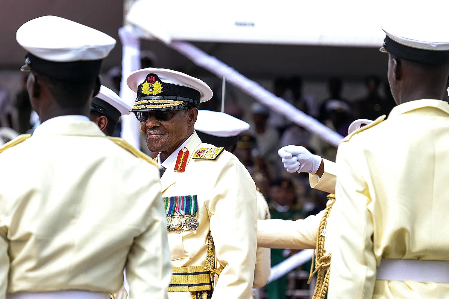 Muhammadu Buhari wears a cream-colored uniform as he looks at others wearing similar garb.
