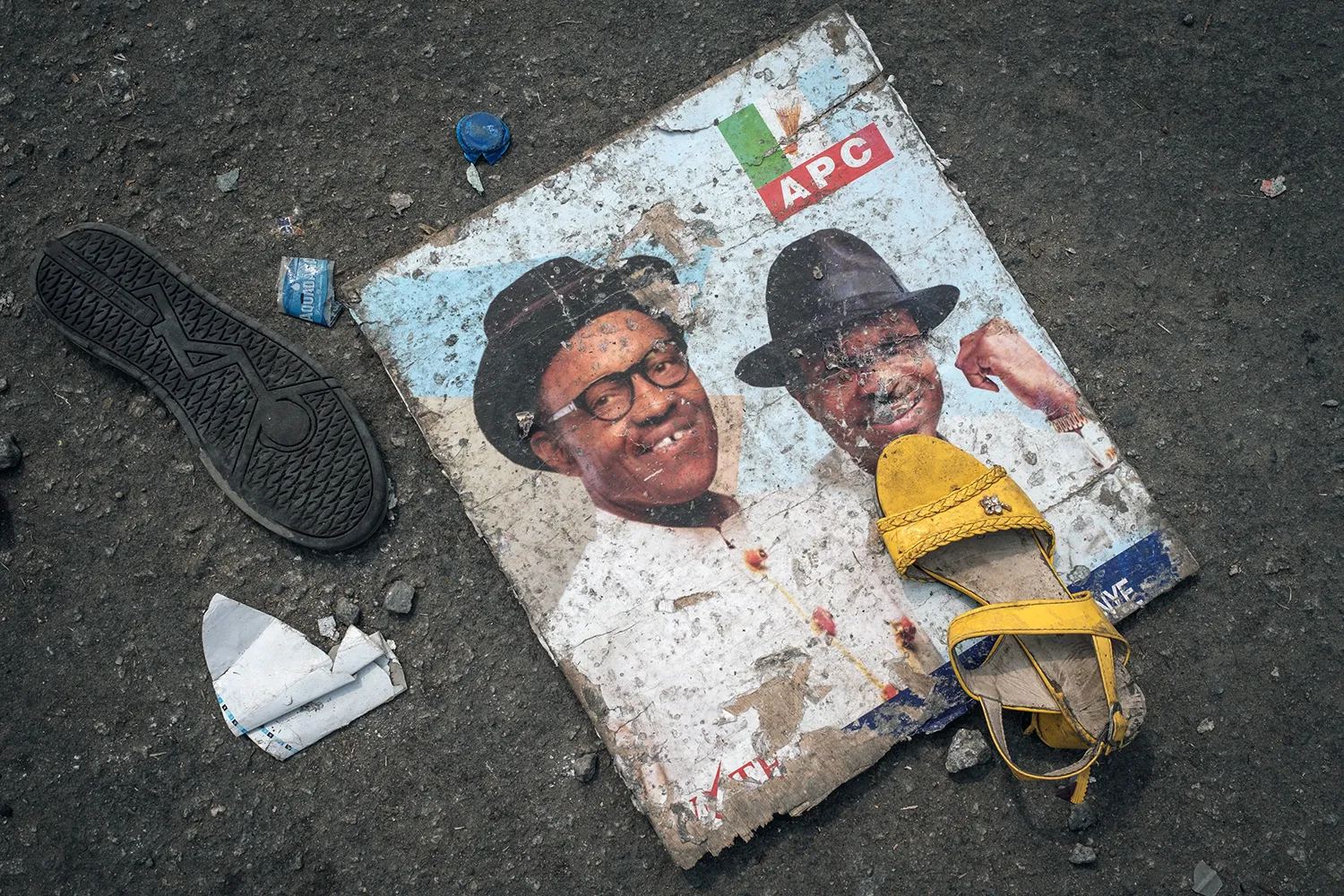 A scuffed-up political poster and two mismatched shoes appear on a street.