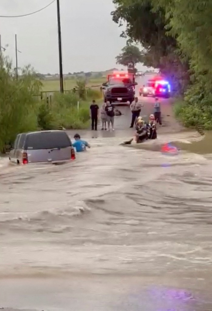 Rescuers assisting a person from a flooded vehicle.