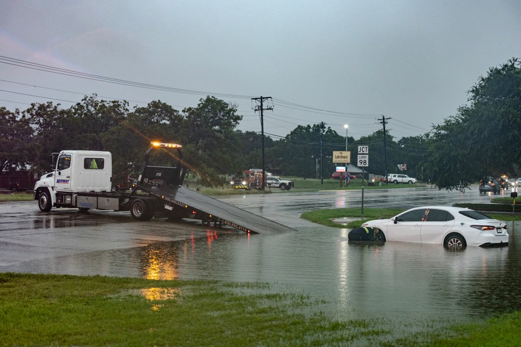 A tow truck driver attempts to recover a submerged car during flash flooding.