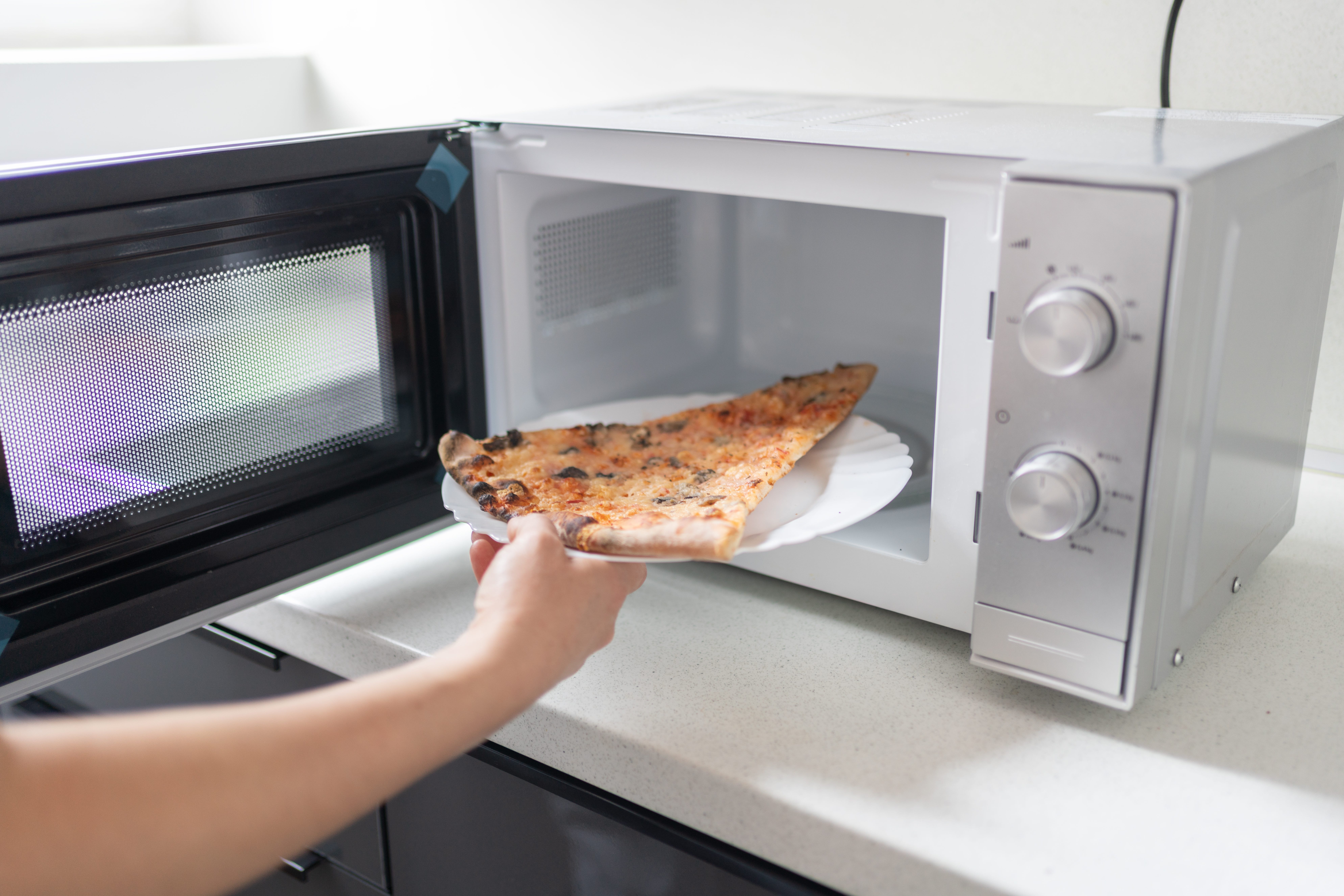 A person puts a slice of pizza in a microwave.
