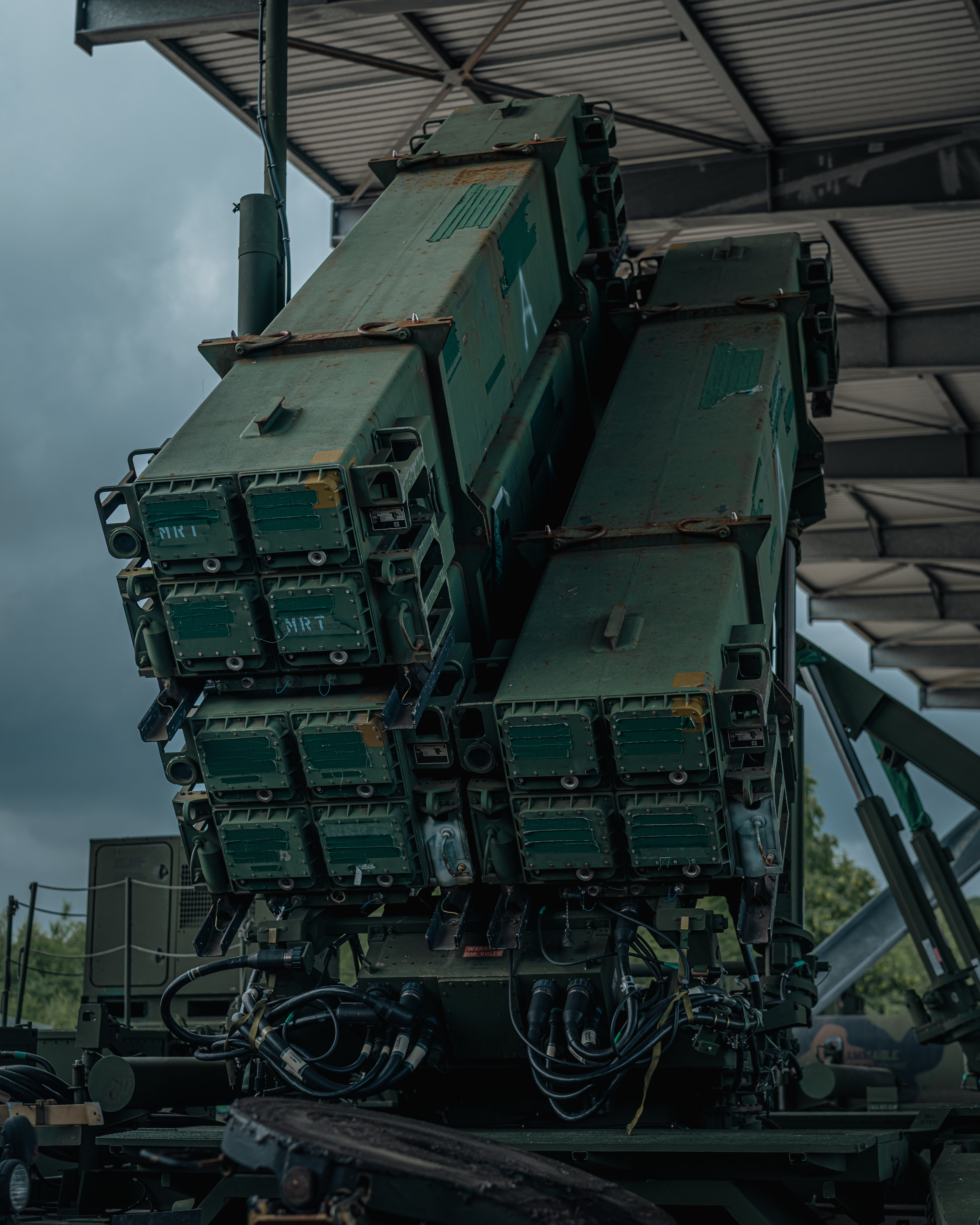 The back of a Patriot missile launcher is seen parked under a structure with a cloudy sky in the background.