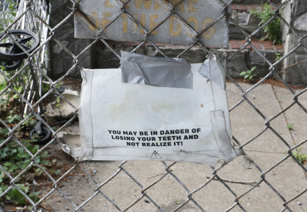 Torn sign on a chain-link fence warning of dog attack.