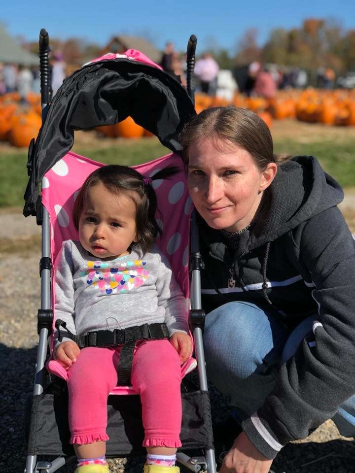 Woman and toddler daughter in stroller at pumpkin patch.