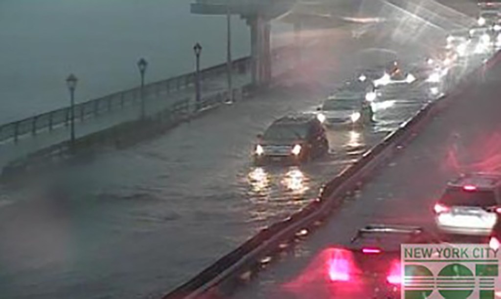 Flooded road in New York City with cars driving through the water.