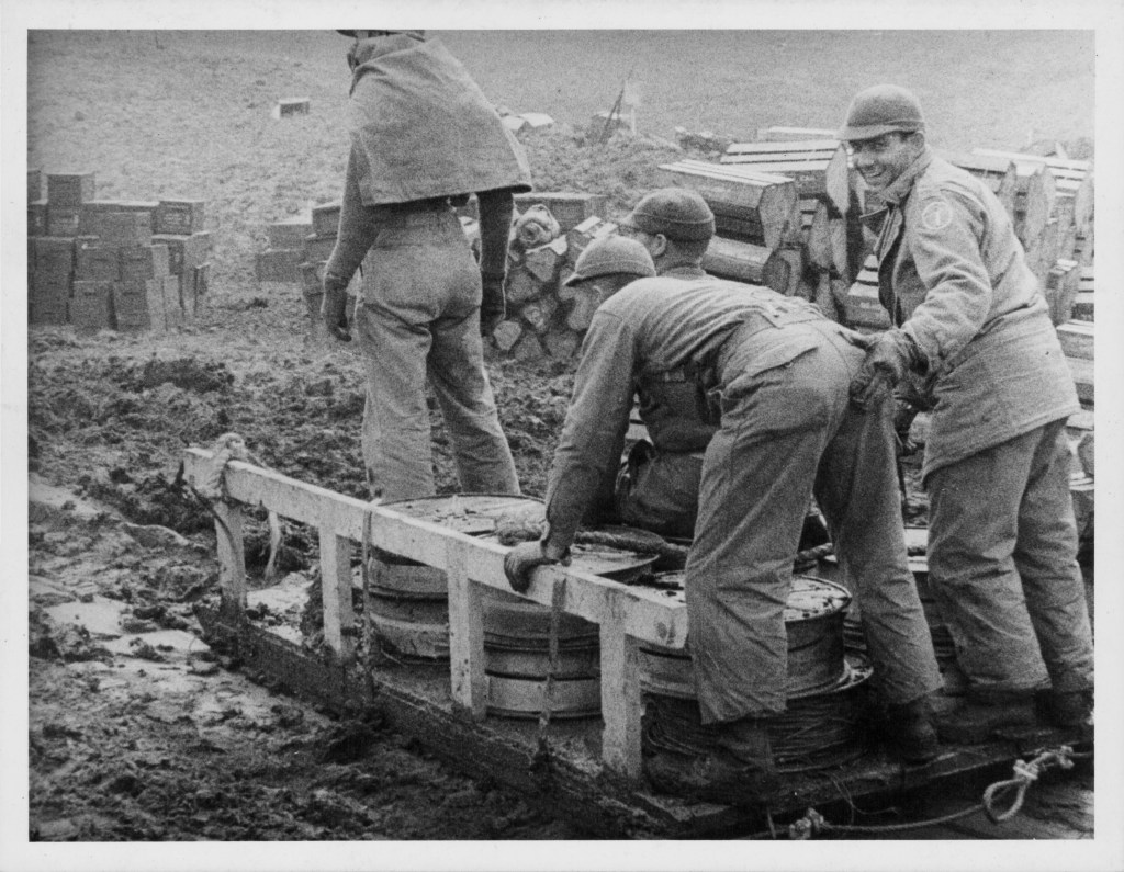 US troops unloading supplies from a cart in muddy terrain.