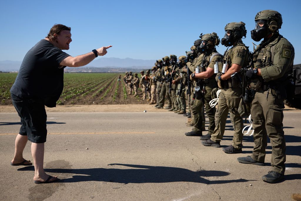 A man gestures toward a line of armed officers in camouflage.