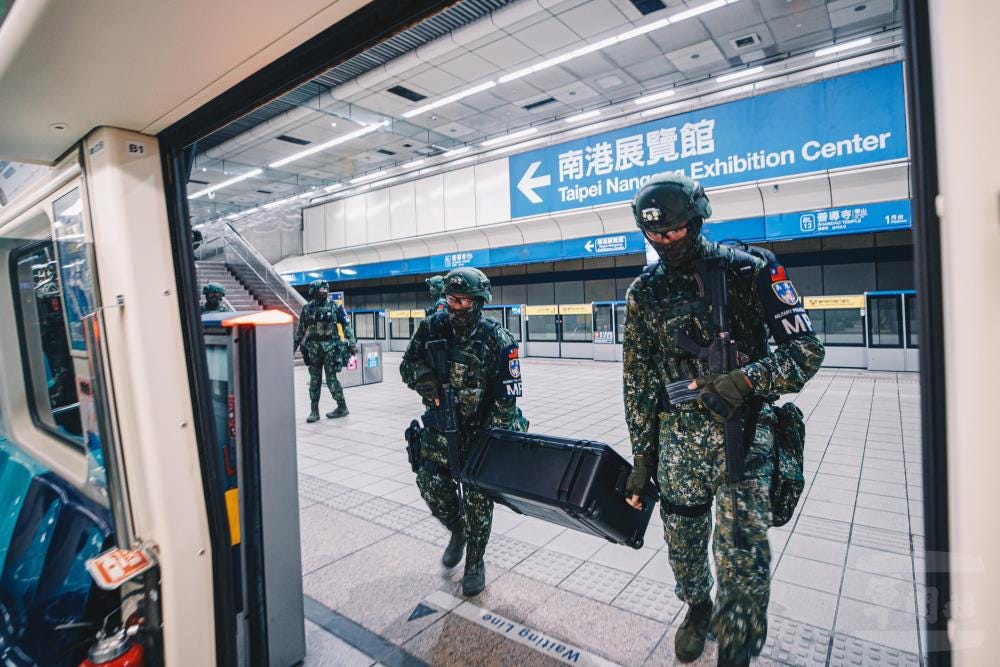 Two armed Taiwanese military police troops carry a case of equipment onto a subway car.