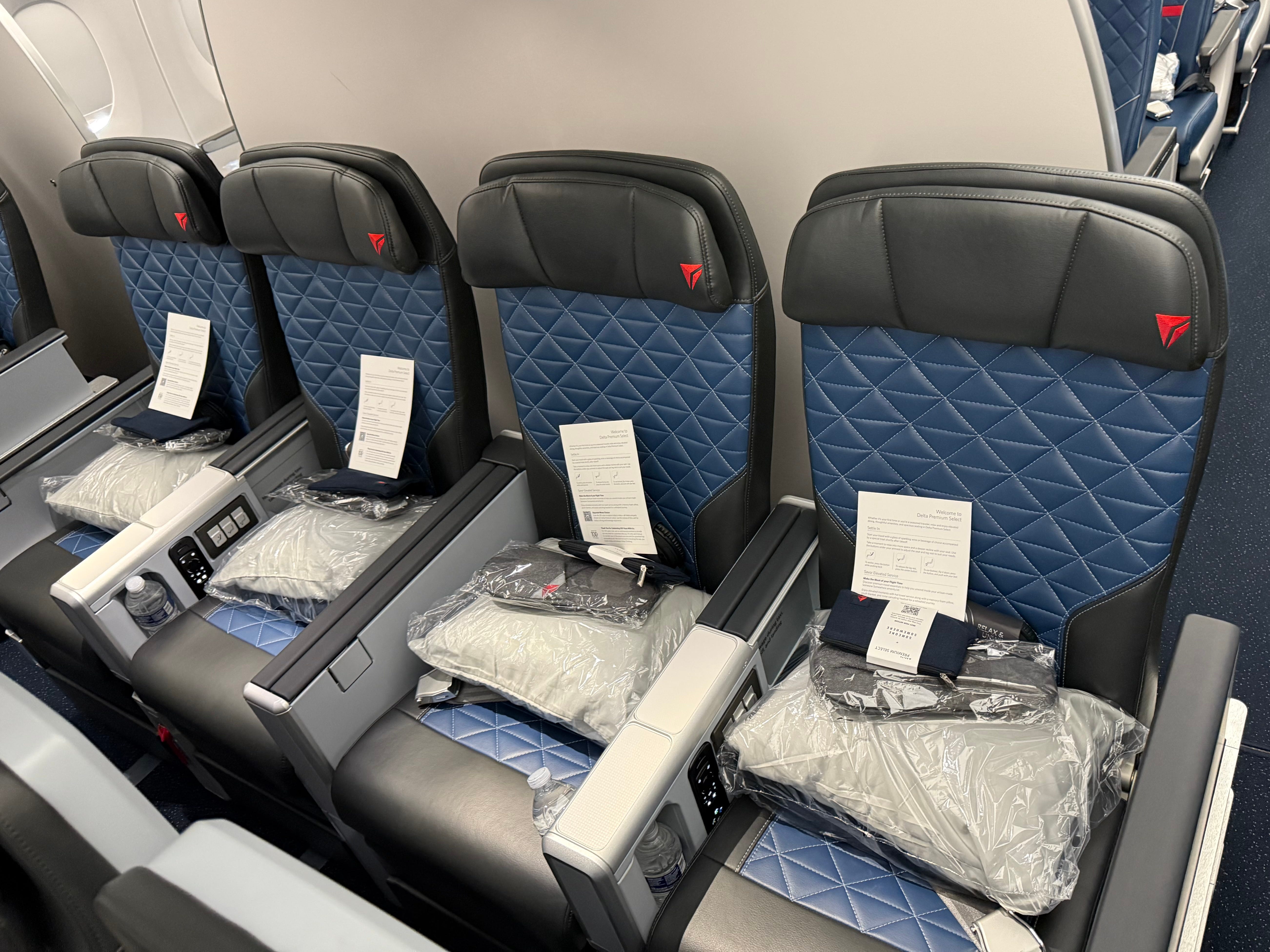 A row of empty seats in Delta's Premium Select cabin. Each seat has a pillow, slippers, and other complementary items.