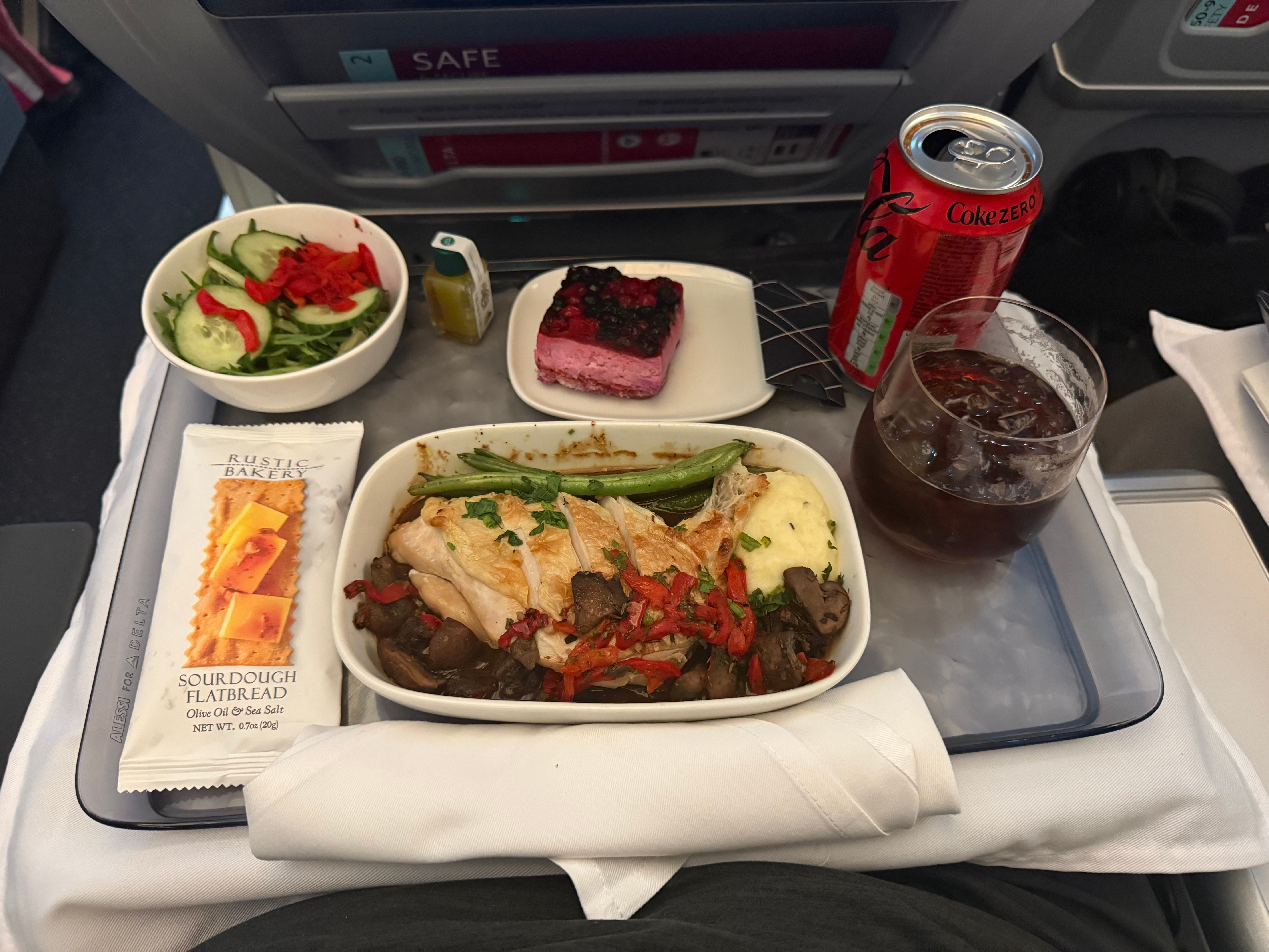 The author's meal on the plane, including a chicken dish, a salad, a dessert, and a Coke.
