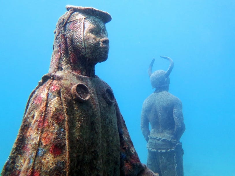 Two underwater sculptures covered in coral.