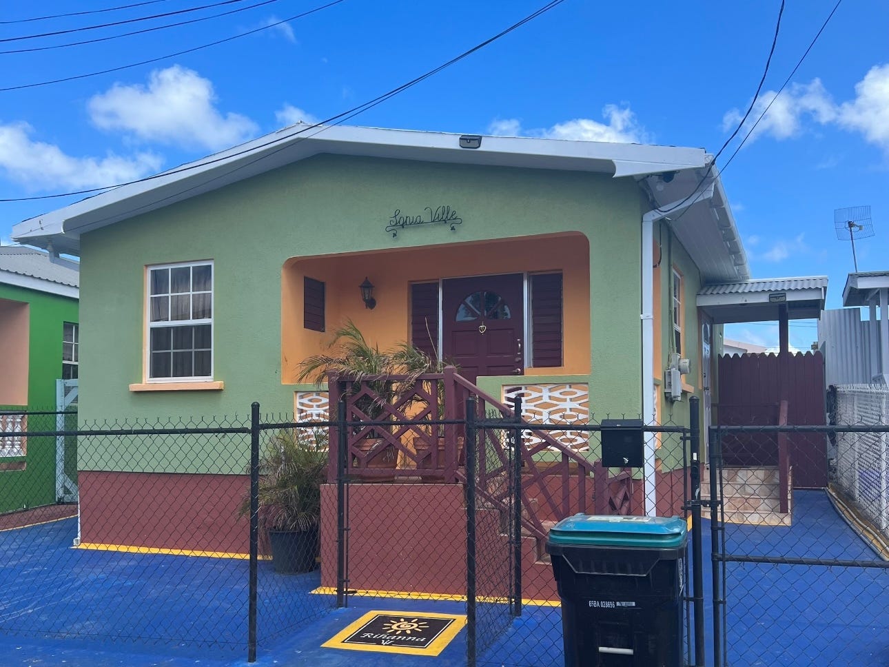 A small colorful house with a fence. The house is green and has yellow and red details.