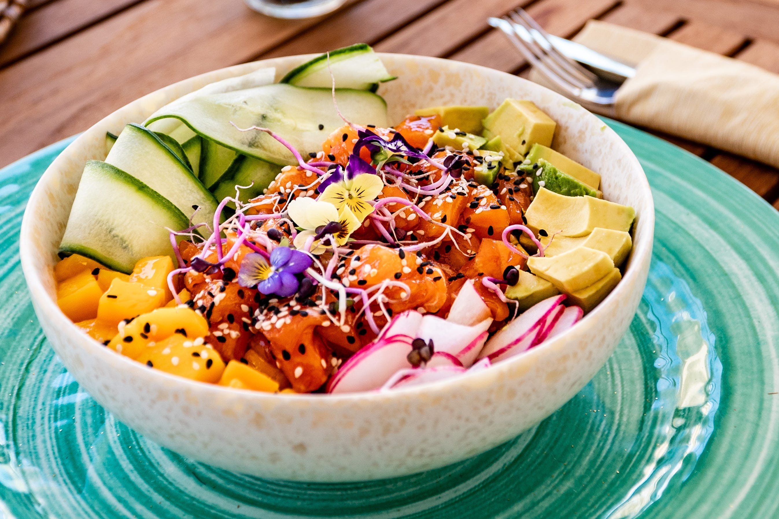 Bowl with salmon, sesame seeds, cucumber on plate