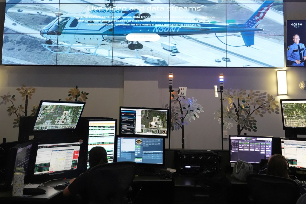 Emergency dispatch center with multiple computer screens displaying live video and data streams.