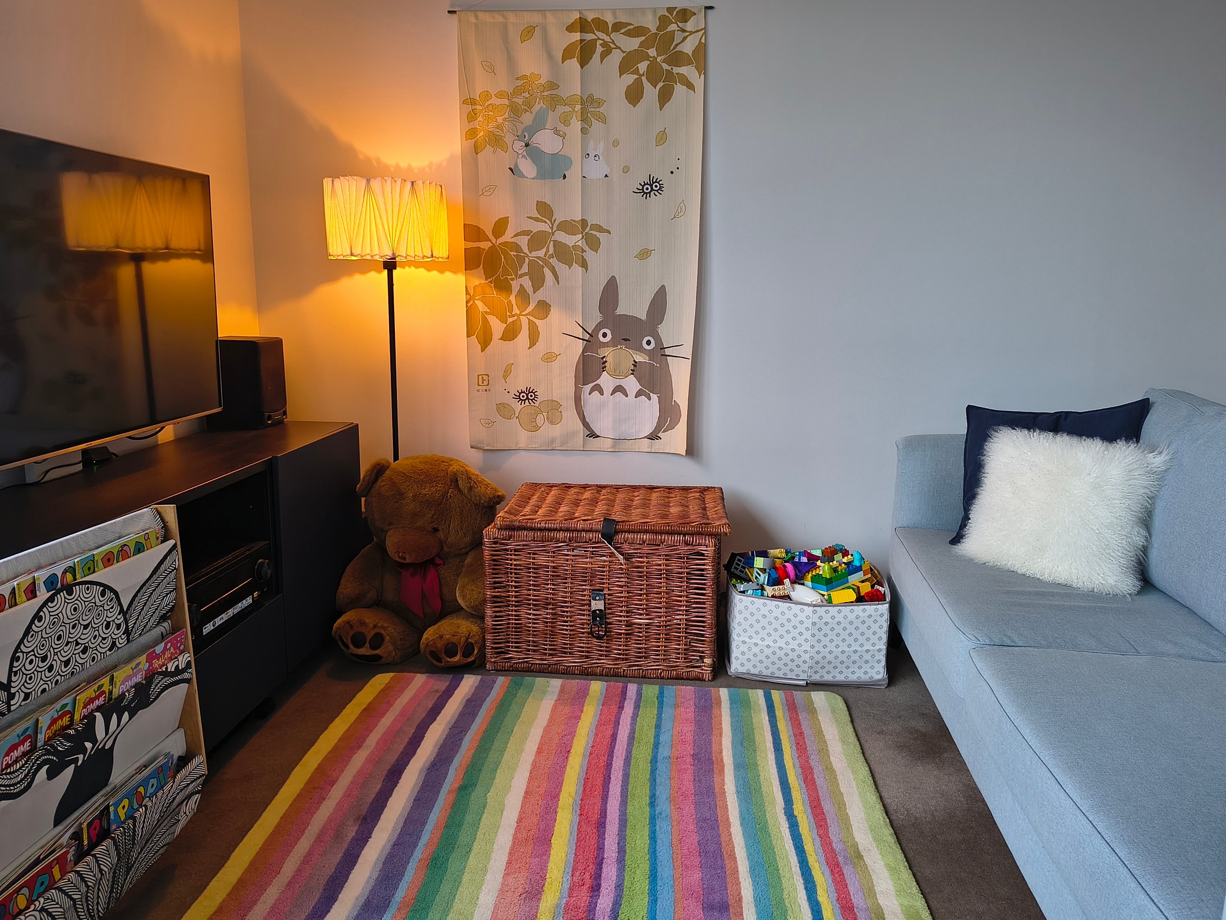 A modest living room with a colorful rug, a gray couch, and baskets containing toys.