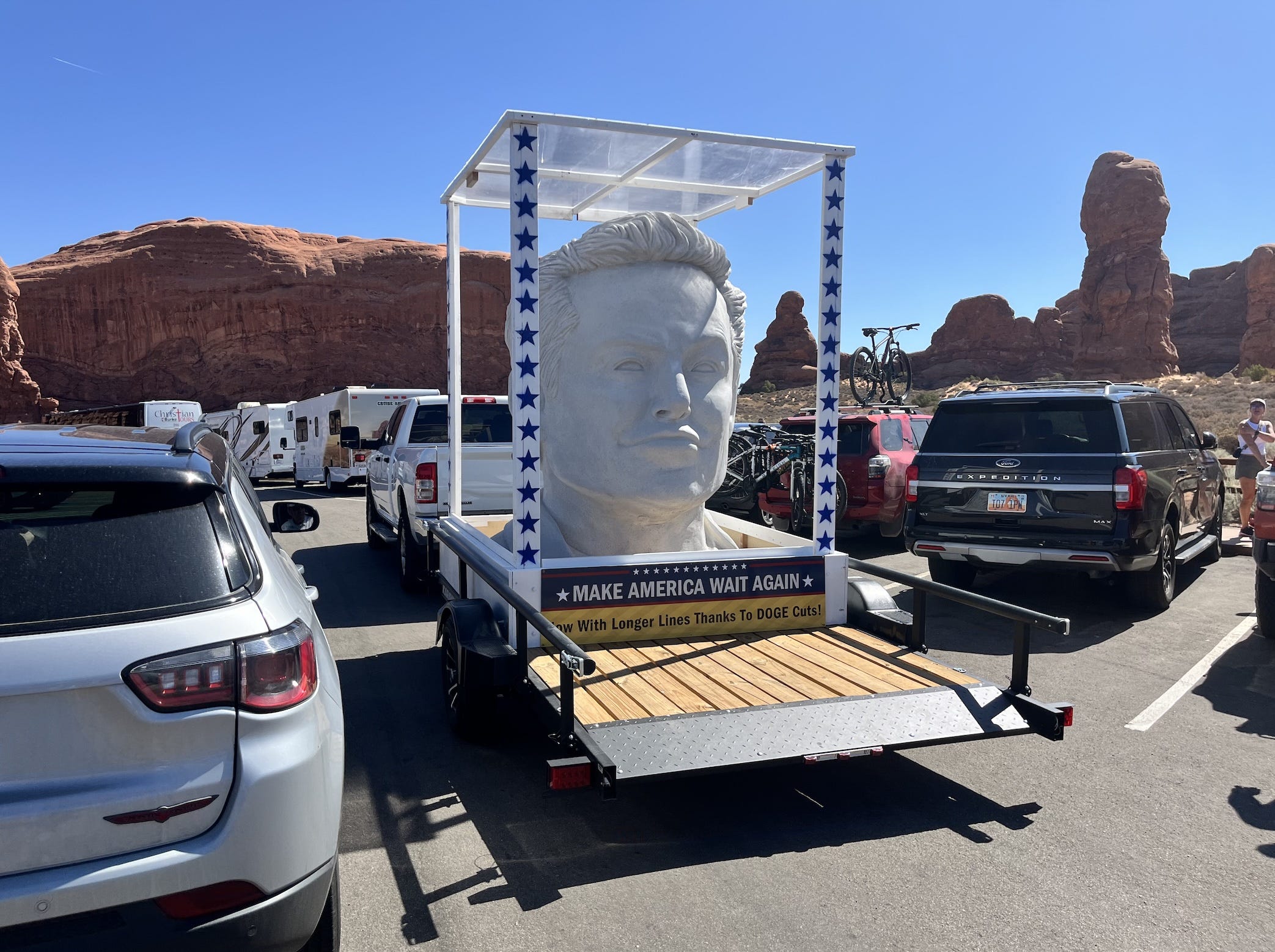 Elon Musk bust on trailer behind pickup driving through Arches National Park.