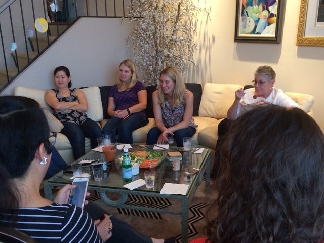 A group sits around a coffee table eating snacks and talking.