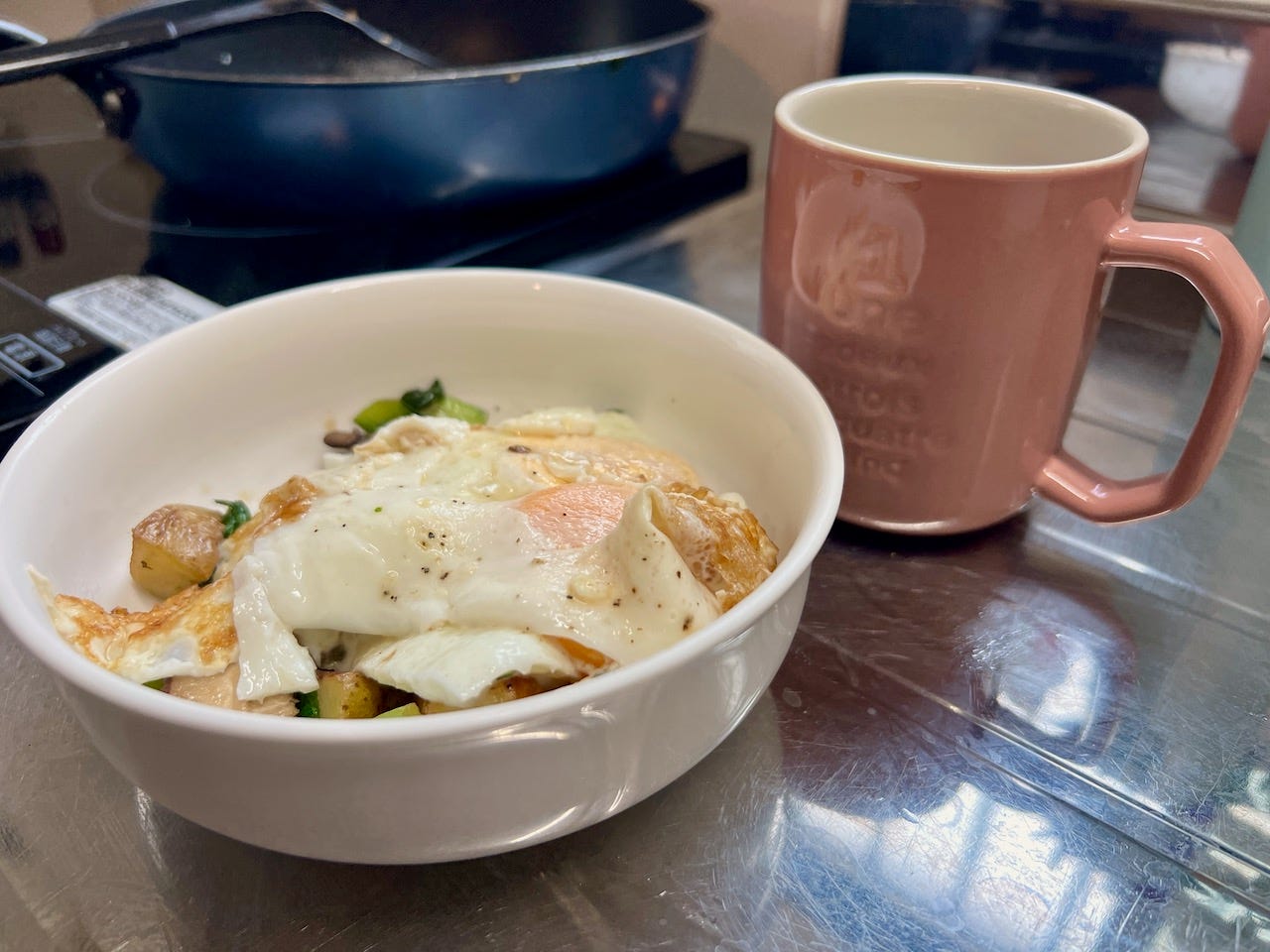 A bowl with eggs, potatoes, and peppers, and a mug.