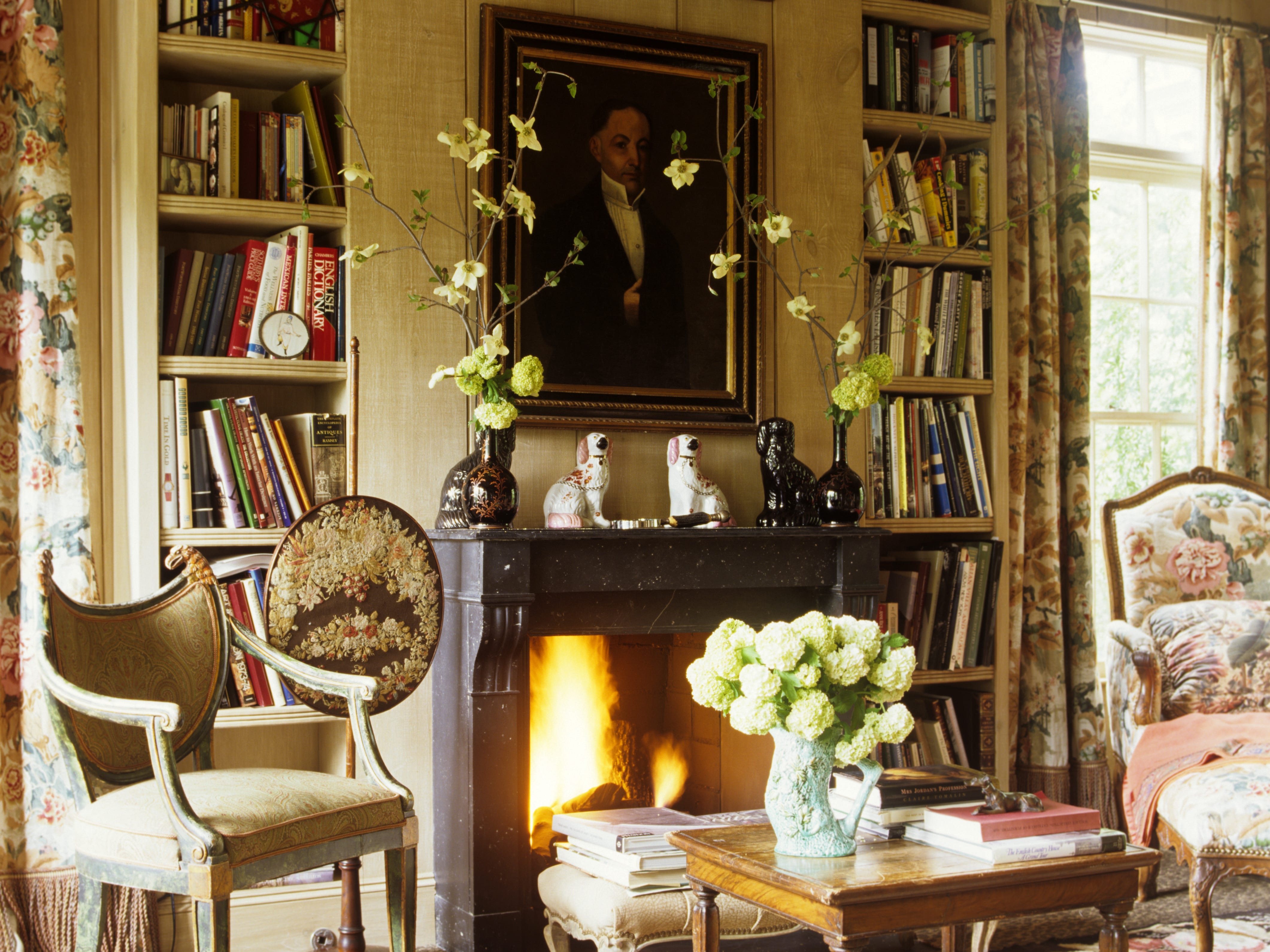 A living room with a fireplace, built-in bookcases, antique chairs, and patterned curtains.