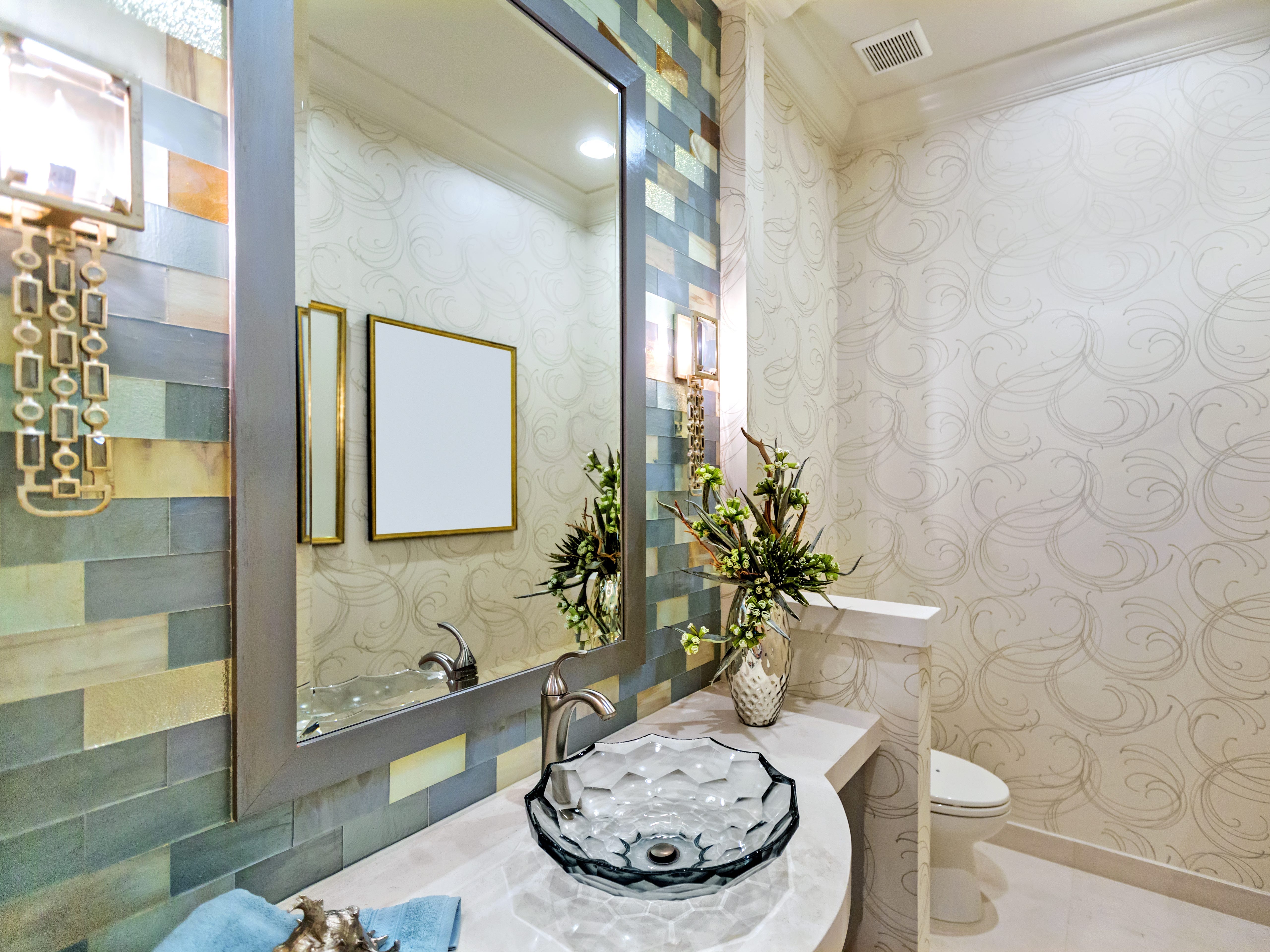 A powder room featuring a wall with yellow, green, and teal tiles and a white wallpaper with gray swirls.
