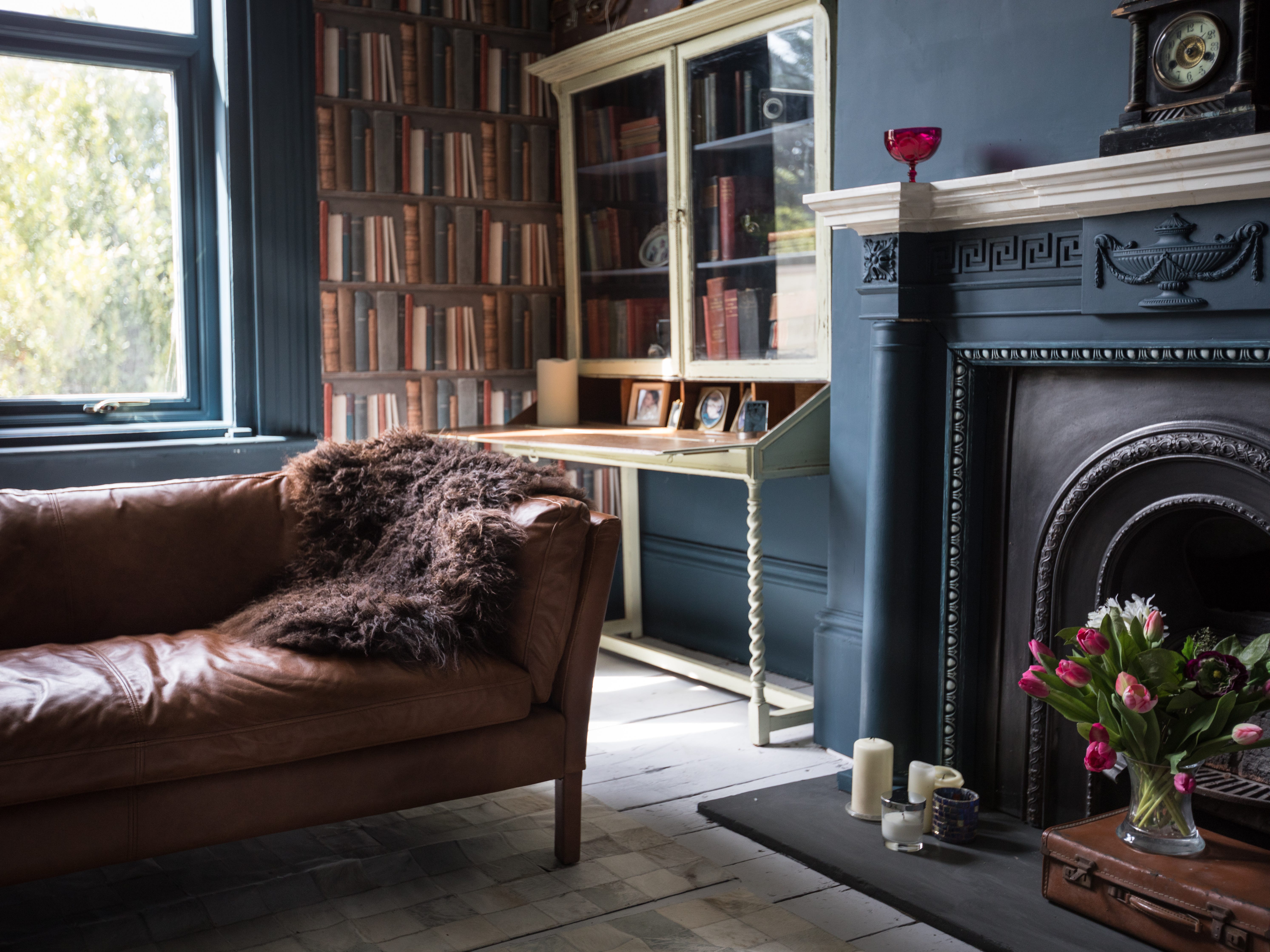 A dark vintage living room with a dramatic fireplace and brown leather couch.