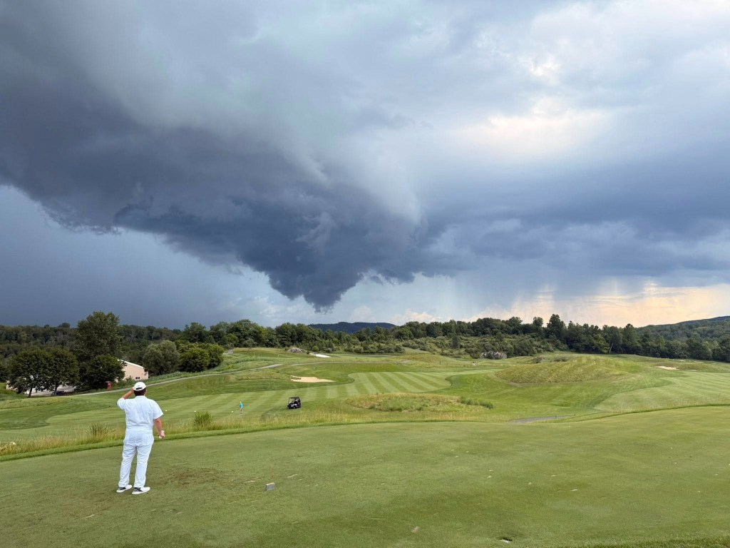 Golfer on a golf course under a stormy sky.