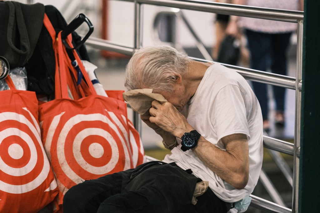Elderly man wiping his face while sitting with shopping bags.