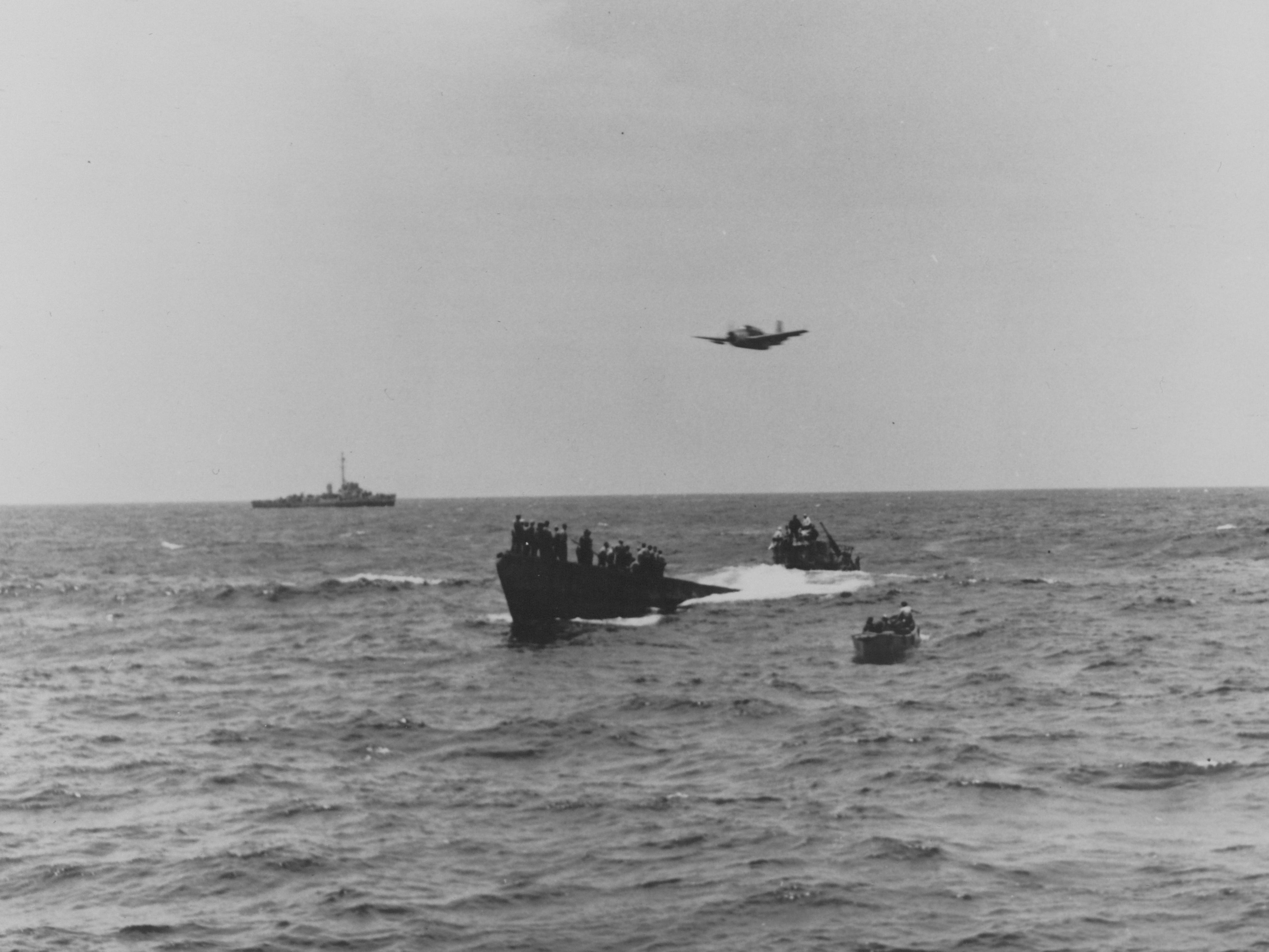 USS Guadalcanal's Turboprop Aircraft (TBM) circles overhead alongside the USS Chatelain, whose depth charge attack forced the German crew to surface and abandon their ship.