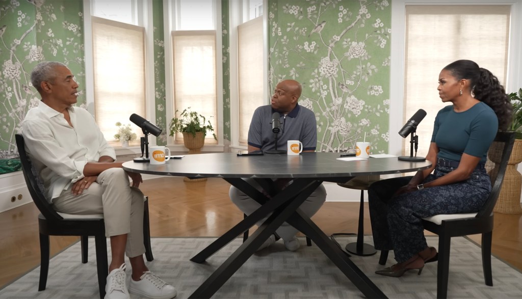 Barack and Michelle Obama and a podcast host sitting around a table during an interview.