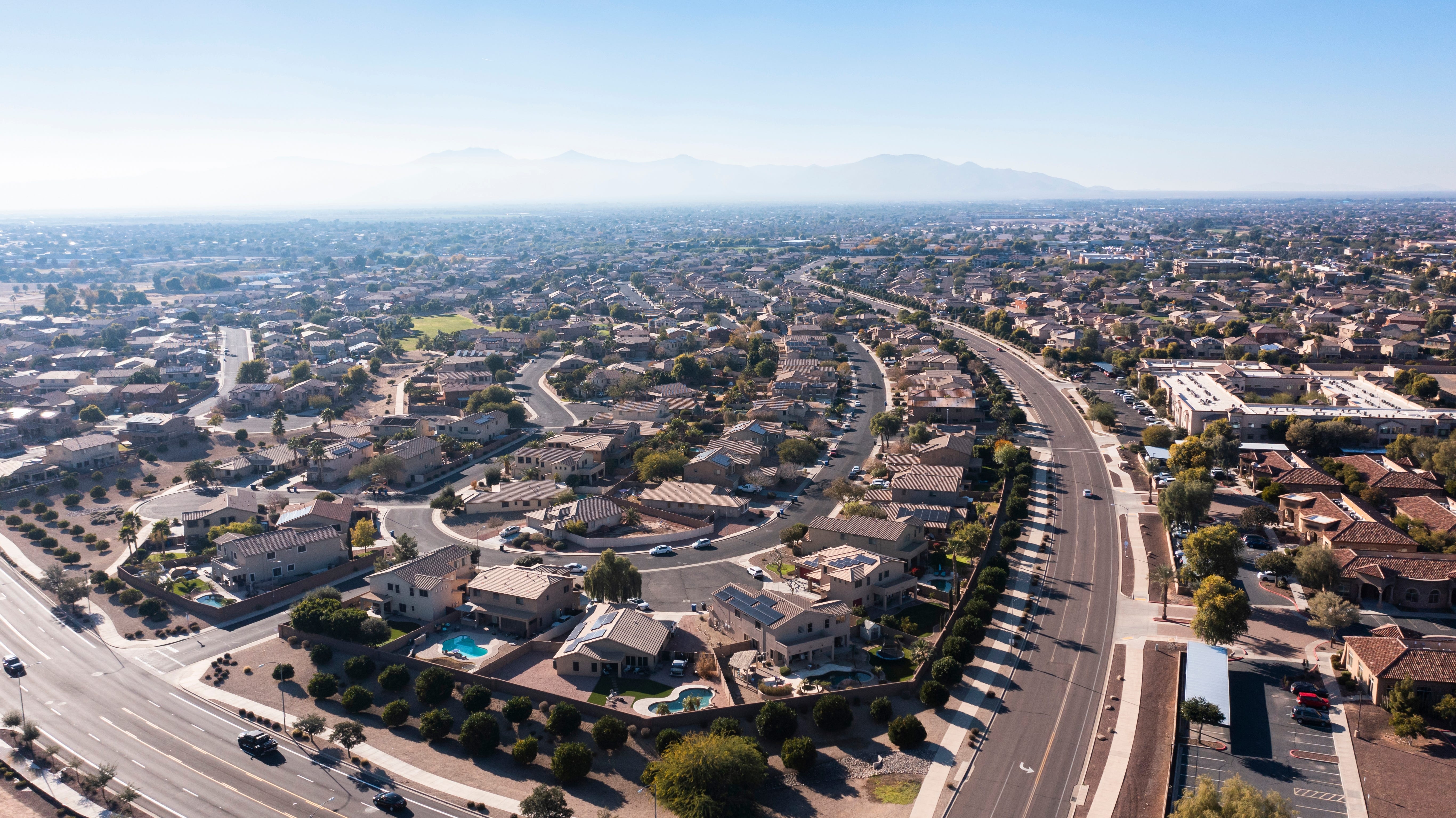 Many homes neatly layed out near a winding roads with mountains in the background