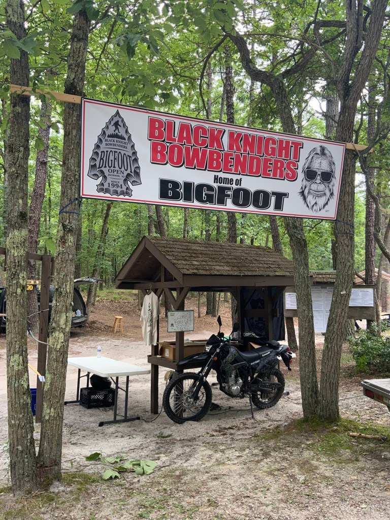 Photo of a Black Knight Bowbenders archery range sign, a motorcycle, and a registration table.