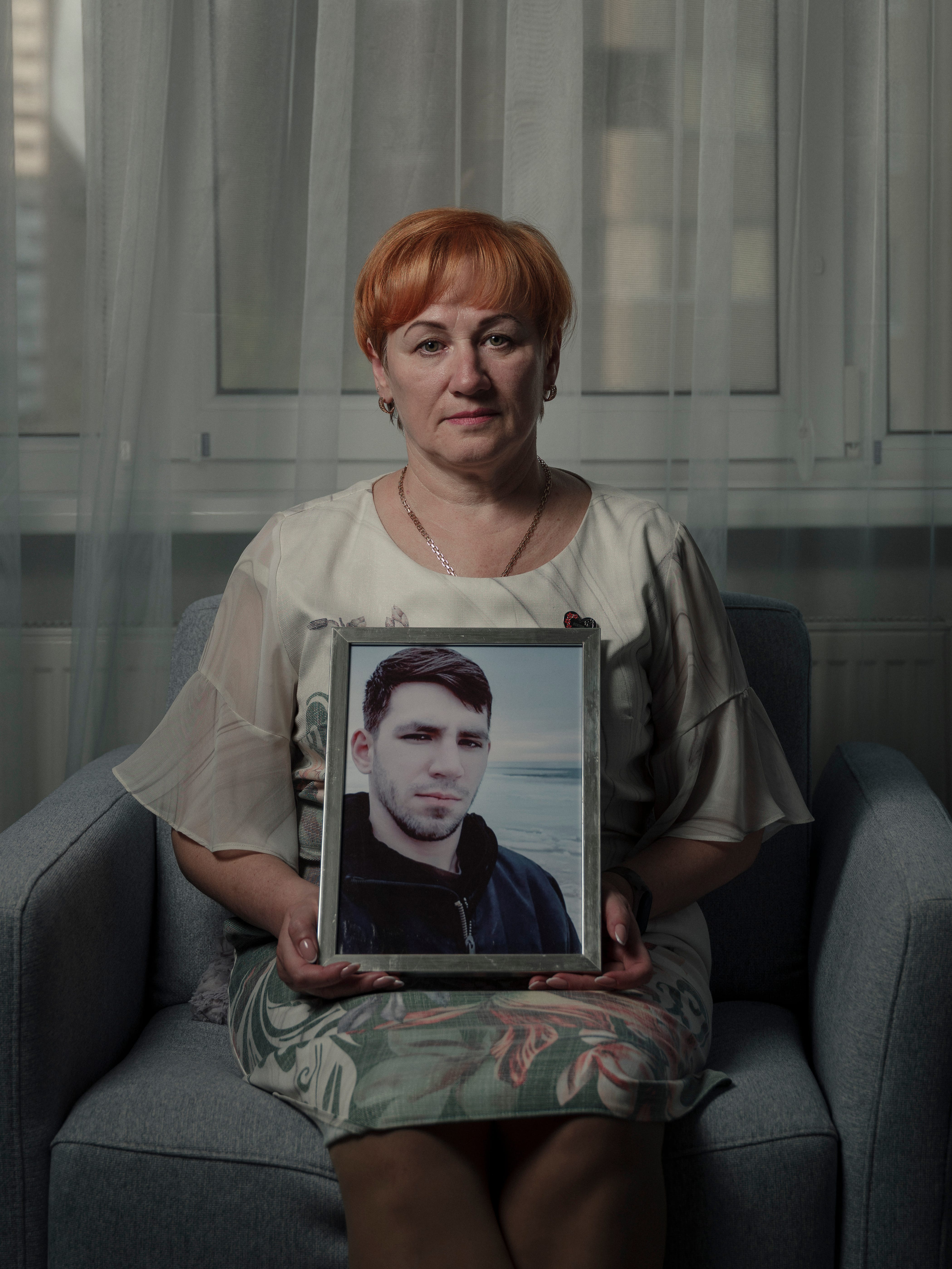 Vira Lytvynenko sits for a portrait in her apartment while holding a photo of her son Vladyslav.